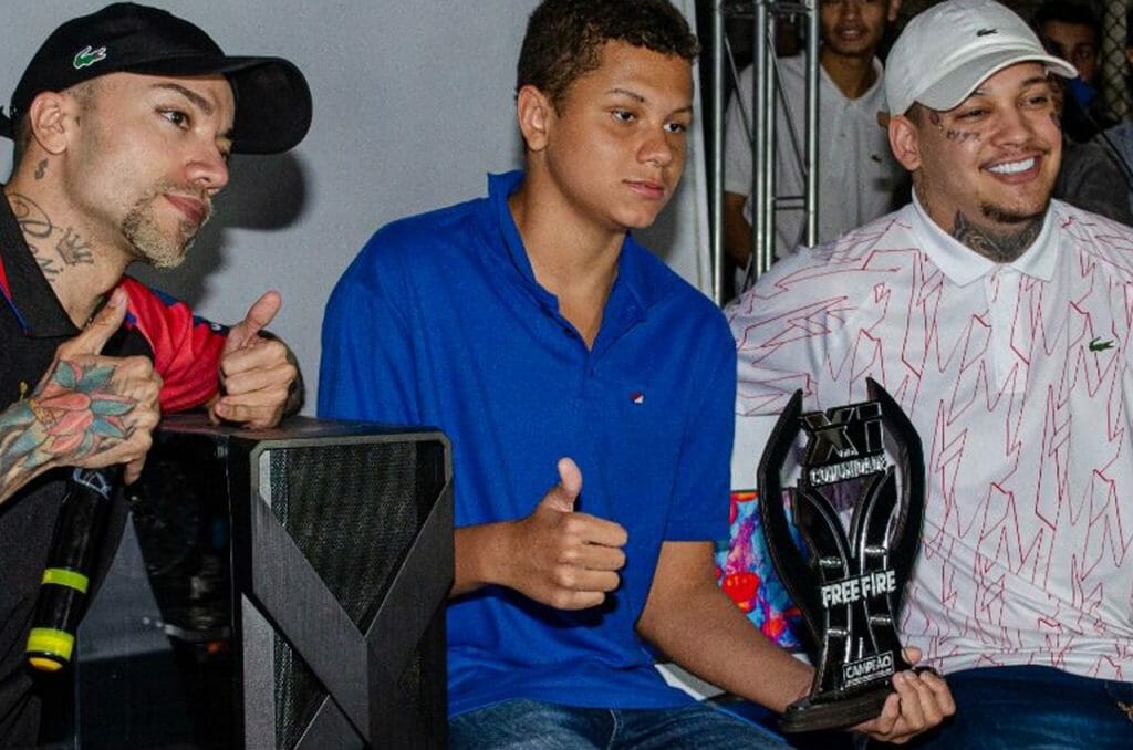 Os influencers @lazarosonicff (esq.) e @dantes.ff (dir.) posam ao lado de participante do evento. (Imagem: Divulgação)